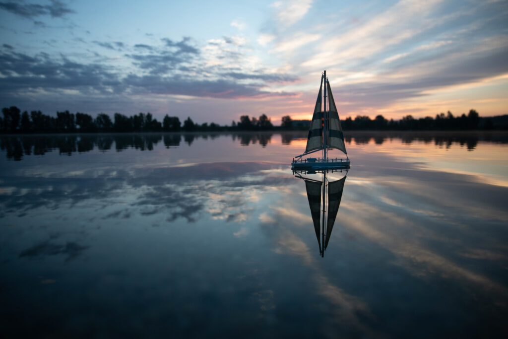 sailboat on a quiet lake reflecting sunrise