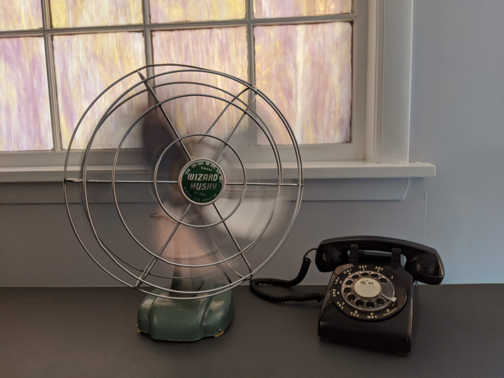 old fashioned fan and rotary dial phone on desk by window