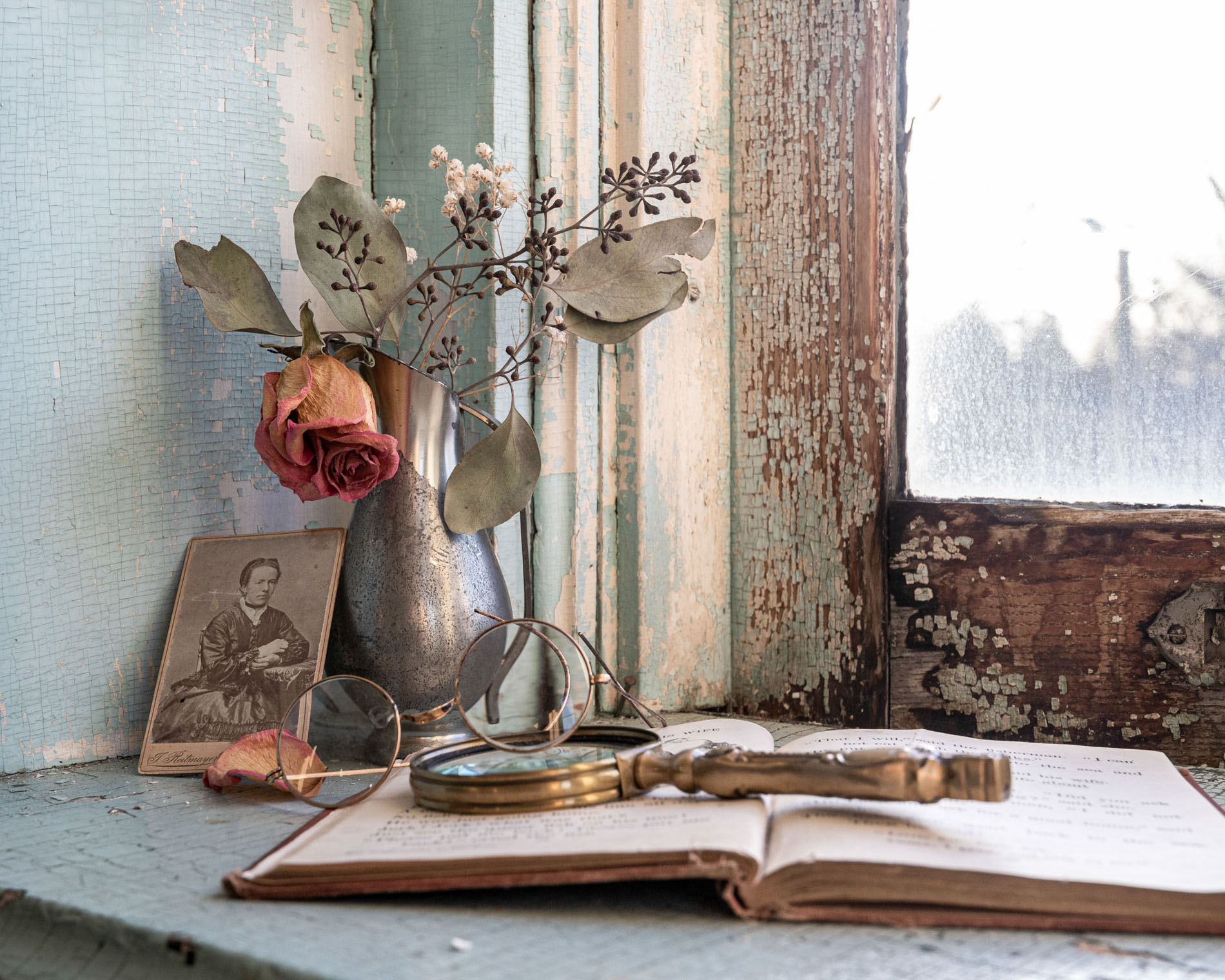 faded rose, photo and antique magnifying glass in front of an old window