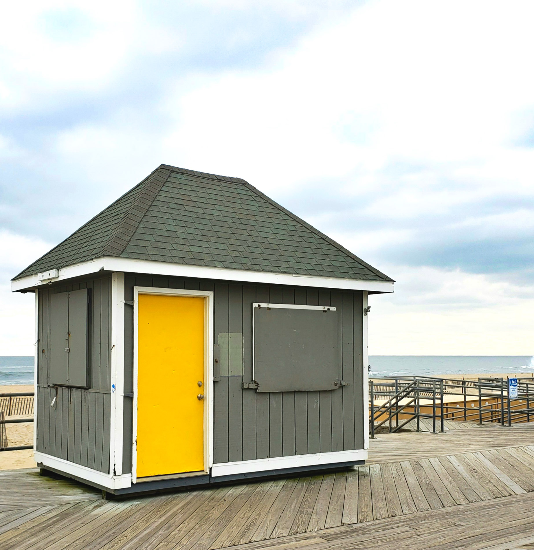 Grey shack with yellow door in front of ocean on partly cloudy day