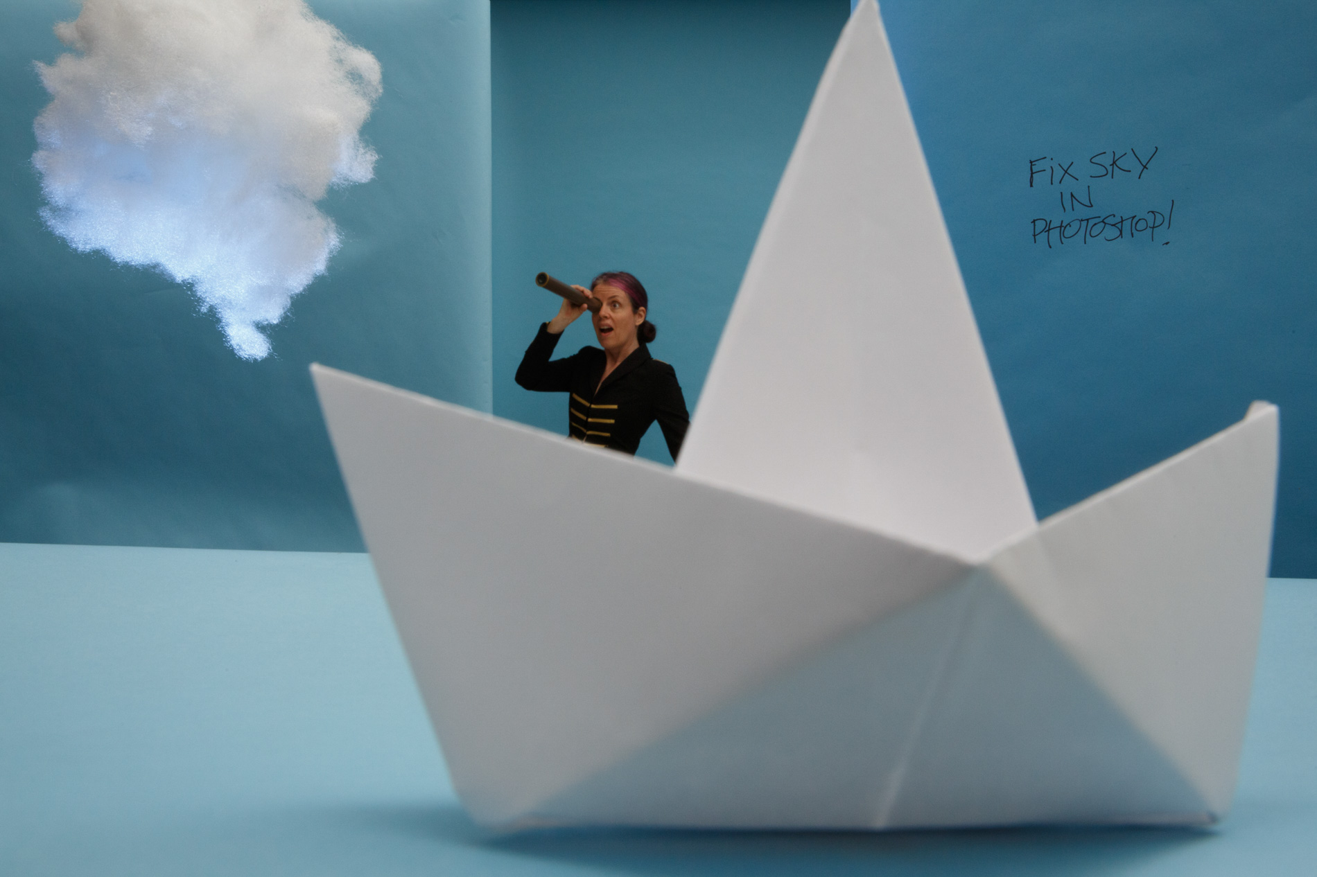 Sam Breach behind a paper sailboat lookint at a cotton cloud through a spyglass