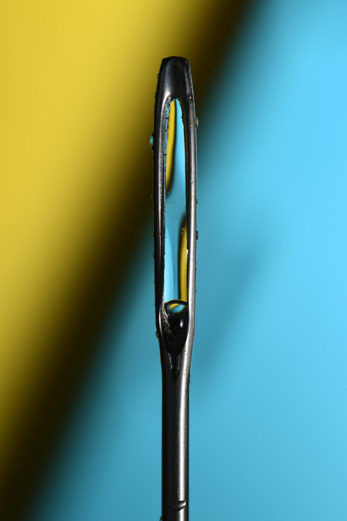 eye of a sewing needle in front of yellow and blue background